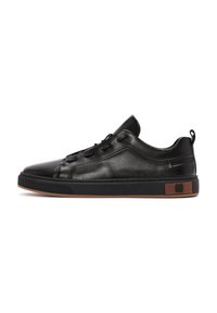 Zapatillas negras de cuero con punta redonda, diseño con cordones, cuello acolchado y suela de goma marrón que presenta un acento de logo en el costado.