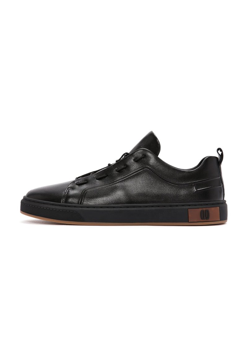Zapatillas negras de cuero con punta redonda, diseño con cordones, cuello acolchado y suela de goma marrón que presenta un acento de logo en el costado.
