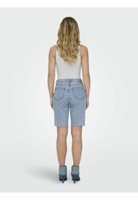 Shorts en denim avec un ourlet effiloché, couleur bleu clair, et design à cinq poches, associés à des bottines à talons gris. Tissu lisse avec un léger élasticité.