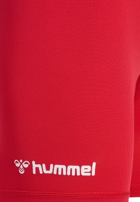 Rote Sportkurze aus glattem, dehnbarem Material, mit einem weißen "hummel"-Logo am unteren Rand und einem figurbetonten Design.