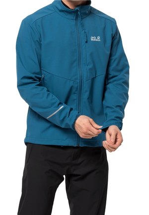 Personne portant une veste bleu Jack Wolfskin ajustant la manche, associée à un pantalon noir, sur fond blanc.