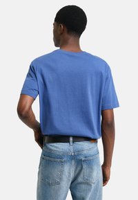 Blå bomulls-T-shirt med kort ärm och rund halsringning, tillsammans med ljusblå denimjeans. T-shirten har en slät yta.