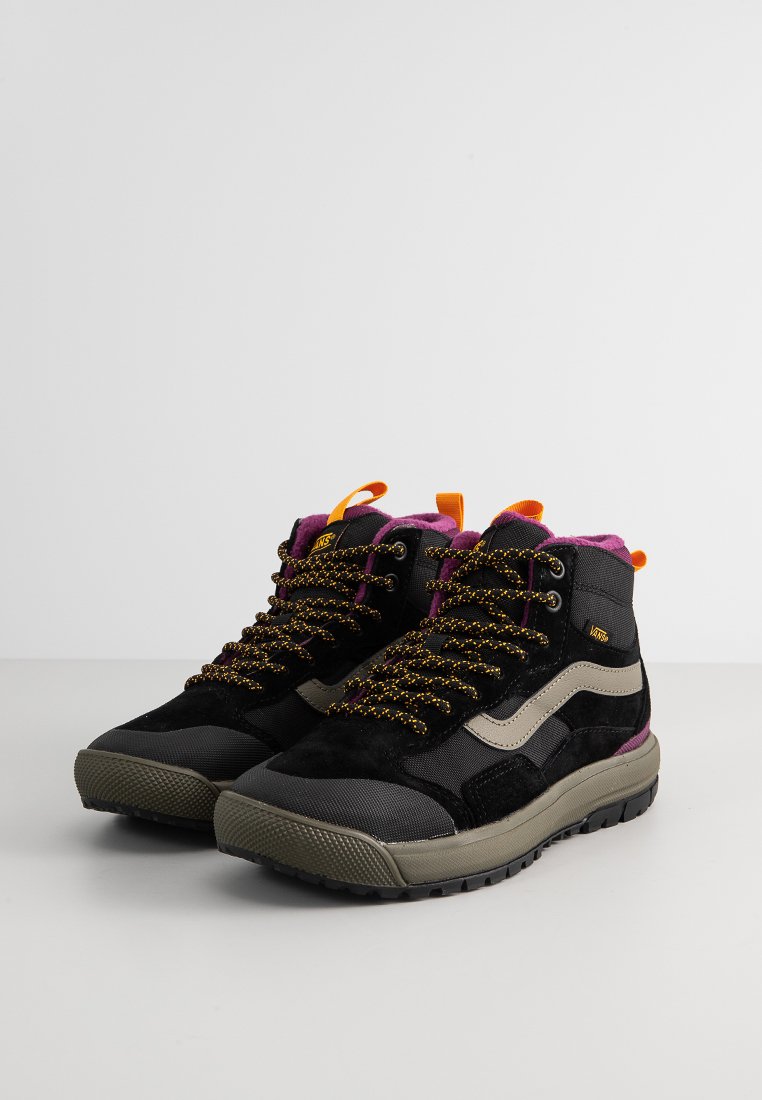 Zapatillas mid-top en negro y gris con materiales texturizados, cordones amarillos y morados, y una suela beige. Presenta un logo y acentos en contraste.