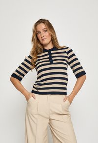 Stribet polo-shirt i marineblå og beige med tre-knaps lukning, korte ærmer og en tætsiddende pasform, kombineret med beige bukser med høj talje.