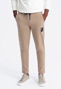 Beiga joggerbyxor i mjukt material med slim fit, med sidorfickor, dragsko i midjan och en liten svart etikett på vänster lår.