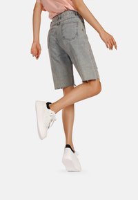 Bermuda in denim lavaggio chiaro con orlo sfilacciato, cinque tasche e vestibilità rilassata. Combinati con scarpe da ginnastica bianche con dettagli neri.