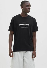 Sort bomulds T-shirt med kortærmer, med et sølvfarvet grafisk tryk "JACK & JONES" centreret på fronten. Rund halsudskæring.
