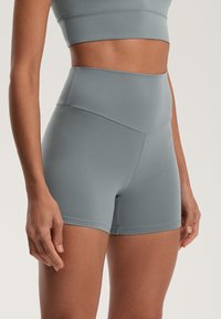 Vysokokréne fitnes šortky v mäkkej šedej látke, s plochými švami a hladkým povrchom, navrhnuté pre pohodlie a flexibilitu.