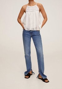 Haut en dentelle blanche à coupe ample avec bretelles réglables, associé à un jean en denim bleu clair évasé avec des fentes latérales aux chevilles.