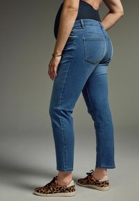 Vaqueros de mezclilla azul de corte ajustado, con bolsillos traseros y una cintura de altura media. Combinados con zapatos de estampado de leopardo y una blusa negra.