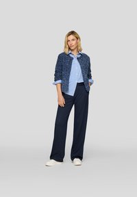 Marineblauer, strukturierten Cardigan über einem hellblau gestreiften Hemd, kombiniert mit marineblauen, gestreiften Hosen und weißen Sneakers. Lässiges Outfit.