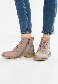 Hnědé semišové kotníkové boty s šněrováním, bočním zipem a plochou gumovou podrážkou. Texturované akcenty a kontrastní švy.