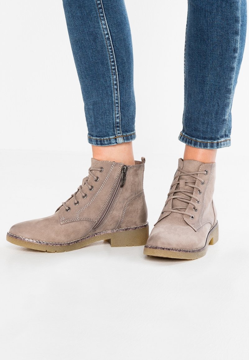 Bottines en suède marron avec un design à lacets, fermeture éclair sur le côté et semelle en caoutchouc plate. Détails texturés et coutures contrastantes.