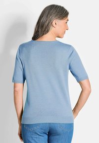 Hellblaue Kurzarmstrickjacke mit rundem Ausschnitt und geripptem Saum. Weicher Stoff, taillierte Passform und minimale Nähte auf der Rückseite.
