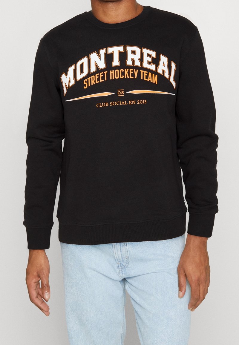 Felpa nera con la scritta "MONTREAL STREET HOCKEY TEAM" stampata in bianco e arancione. Presenta un collo rotondo e polsini a costine. Vestibilità casual.