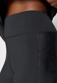 Close-up of a person wearing black high-waisted athletic leggings with visible stitching and a side pocket.