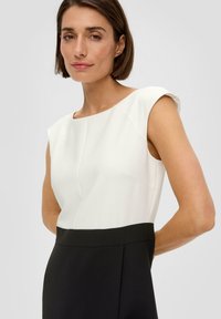 Robe sans manches avec un haut blanc en tissu structuré et une jupe plissée noire. Texture lisse avec un col haut et des lignes nettes.