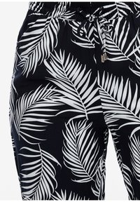 Svarta tygbyxor med ett vitt palmbladsmönster, elastisk midja med dragsnodd och mjukt material.