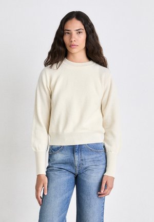 Cream sweater with ribbed neckline and cuffs, featuring a soft texture and slightly puffed sleeves. Paired with blue high-waisted jeans.