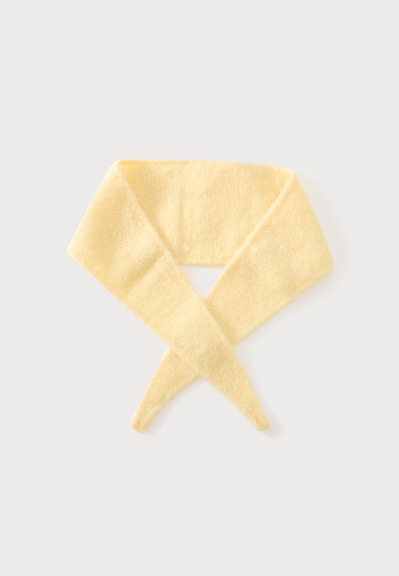 Écharpe tricotée jaune pâle douce avec des extrémités pointues, croisée sur un fond uni gris clair.