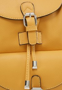 Sac en cuir jaune texturé avec boucle argentée et fermetures à cordon, montrant des coutures détaillées et des embouts métalliques sur les cordons.