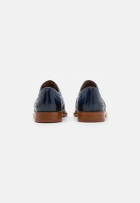 Scarpe eleganti in pelle blu navy con design a punta d'ala, dettagli brogue e suola in legno marrone, viste da dietro.