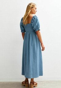 Blå, medellång klänning med puffärmar, smockad livstycke och fyrkantig rygg. Kombinerad med bruna platåsandaler och minimala accessoarer.