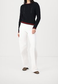 Marinblå kabelstickad tröja med röd och vit randig detalj vid halsringningen och fållen, kombinerad med vita vida byxor och leopardmönstrade skor.