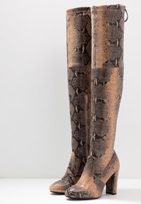 Bottes à talons hauts jusqu'aux genoux avec un motif en cuir de serpent brun et noir, bouts ronds, et fermeture éclair latérale sur fond blanc.