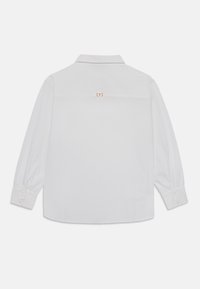 White long-sleeve shirt featuring a folded collar, buttoned cuffs, and a distinctive gold accent on the back. Smooth, textured fabric.