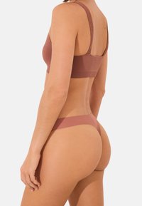 BH- und Tanga-Set aus geripptem pinkfarbenem Stoff. Verfügt über breite Schulterträger und minimalen Rückenschutz. Glatte Textur mit nahtlosem Design.