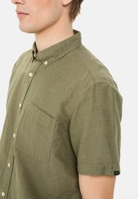 Korte mouwen shirt in olijfgroen stof met een button-down kraag, een enkele borstzak en subtiele stikdetails.