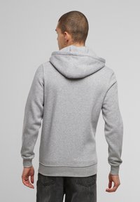 Felpa grigia con cappuccio realizzata in tessuto morbido, dotata di tasca a marsupio e polsini a costine. Il retro presenta un design semplice con dettagli minimi.