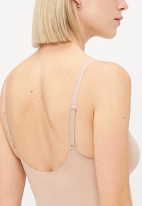 Nude seamless bra with adjustable straps, smooth texture, and a low back design, showcasing soft fabric and minimal hardware detailing.
