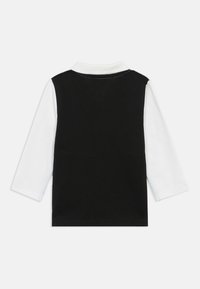 Cămașă cu mânecă lungă alb-negru, având spatele negru, mânecile albe și un guler clasic. Fabricată din bumbac moale, cu detalii de cusătură.