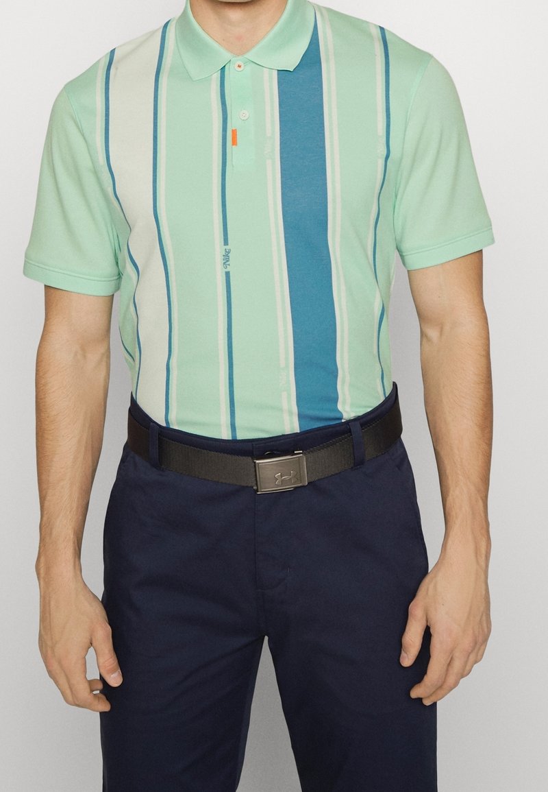 Polo shirt vert clair avec des rayures verticales bleues et blanches, doté d'un col, de trois boutons et d'un petit accent orange. Porté avec un pantalon marine foncé.