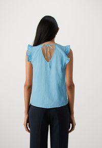 Top senza maniche di colore azzurro chiaro con dettagli arricciati sulle spalle, tessuto texturizzato e schiena con apertura a chiave e chiusura a lacci.
