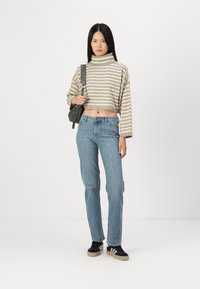 Svītrokota, izgriezta turtleneka džemperis bēšā un pelēkā krāsā; vidēji mazgāti zili džinsi; melnas sporta kedas ar baltām svītrām; neliela plecu soma.