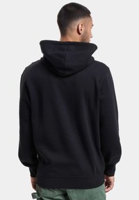 Svart hettegenser laget av bomull med en romslig hette, lange ermer og en avslappet passform. Har et enkelt design og ribbede mansjetter og hem.