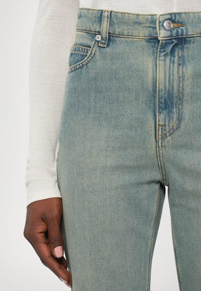 Visoko pasovane svetlo modre denim hlače z rahlim zbledetjem in oranžnim šivanjem, vključujejo kovinsko zaklepanje in stranske žepke.