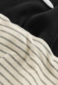 Tissu noir et crème à rayures avec une texture en tricot ; le côté crème présente de fines rayures noires, tandis que le côté noir est lisse et uni.
