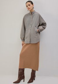 Prevelika svetlo siva jakna z ovratnikom, zapenjanjem na gumbe in elastičnimi manšetami, združena z rebrasto rjavkasto krilo srednje dolžine in rjavimi škornji.