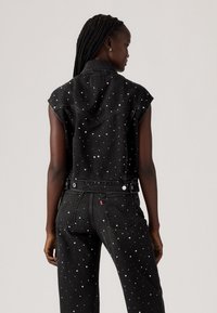 Zwarte denimjack met schouderflappen, voorzien van metalen studs. De achterkant toont een slim-fit ontwerp en een klassieke kraag.
