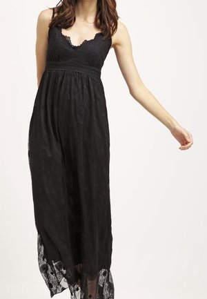 Czarna długa sukienka z koronkowym górnym panelem, dekoltem z falistymi krawędziami oraz teksturowaną kwiatową nakładką. Rękaw wykończony przezroczystą koronkową lamówką.