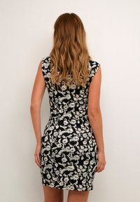 Robe à motifs floraux avec une base noire, présentant des dessins blancs et bleus. Manches courtes style cap et coupe ajustée qui met en valeur sa silhouette.