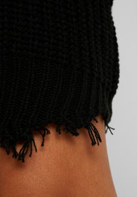Top nero a maglia con design a coste e orlo sfrangiato. Morbido al tatto con linee verticali e fili sciolti lungo il bordo inferiore.