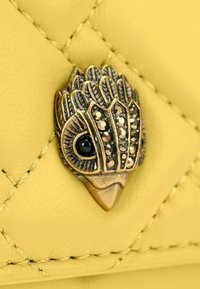 Geel, gestikte leer met een metallic vogelvormig accessoire voorzien van zwarte en zilveren versieringen en verfijnde details.