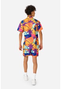 Farverigt sæt med kortærmet skjorte og shorts med mønstre af palmer og geometriske figurer i orange, pink, blå og lilla nuancer.