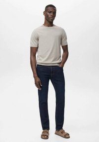Camiseta de manga corta gris claro, jeans azul oscuro y sandalias marrones. La tela parece suave; los jeans tienen un corte clásico con cinco bolsillos.