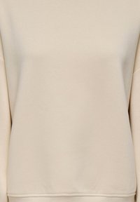 Sweatshirt beige à manches longues avec poignets et ourlet côtelés, présenté sur un fond neutre.